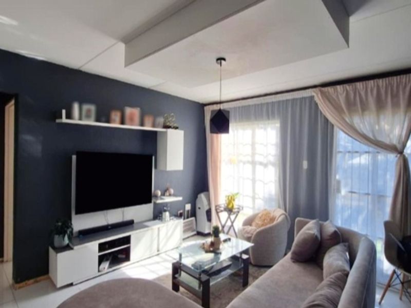 A well-lit living room featuring a dropped ceiling detail, pendant lighting, and a built-in media console against a dark accent wall.