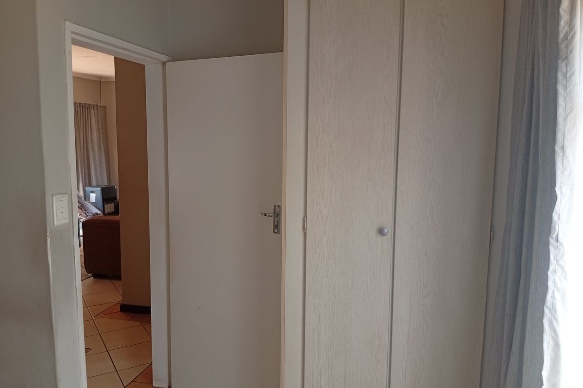 A bedroom interior featuring a built-in wardrobe and a doorway leading to an adjacent living area with tiled flooring.