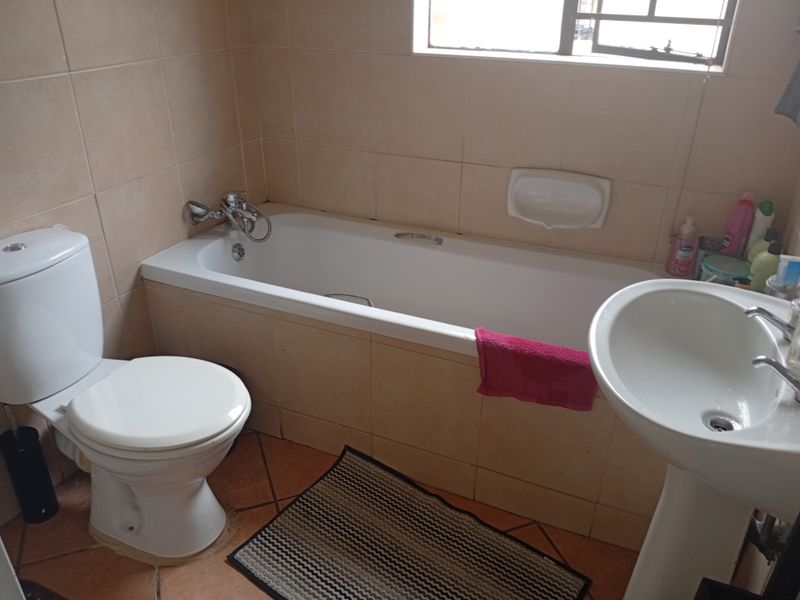 A functional bathroom featuring a bathtub, pedestal basin, and toilet with neutral wall tiling and terracotta-style floor tiles.
