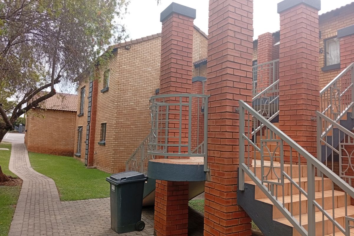 Exterior view of a townhouse complex featuring face-brick construction, external tiled staircases with metal railings, and a paved walkway through the garden area.