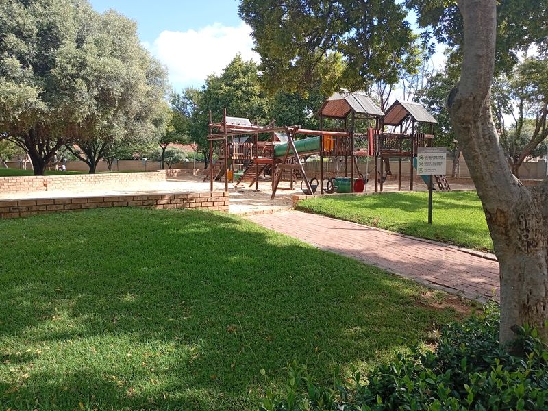 A well-maintained communal playground area featuring wooden play structures, brick retaining walls, and landscaped green spaces within the townhouse complex.