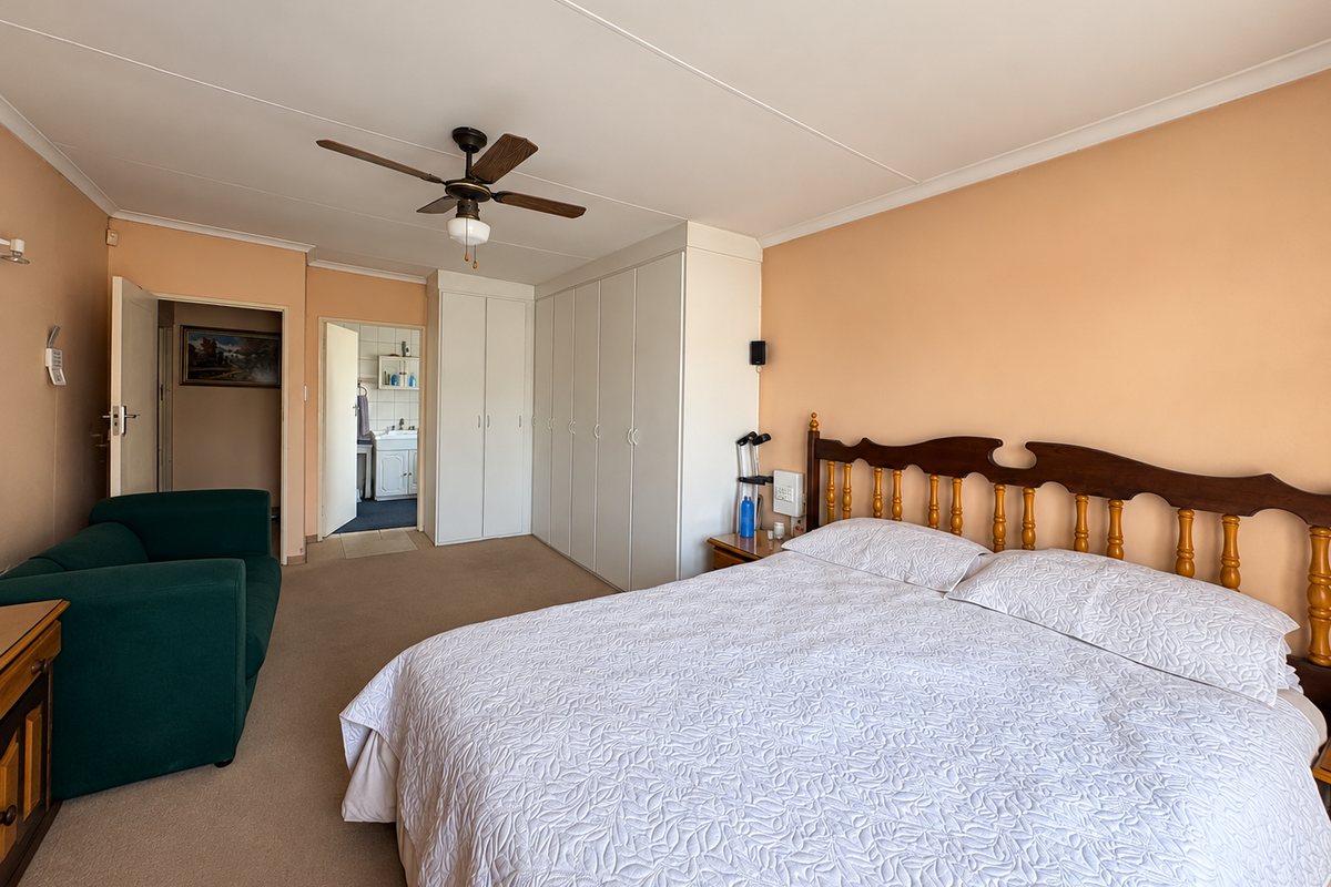 Spacious bedroom featuring built-in cupboards, a ceiling fan, neutral carpeting, and direct access to an en-suite bathroom.