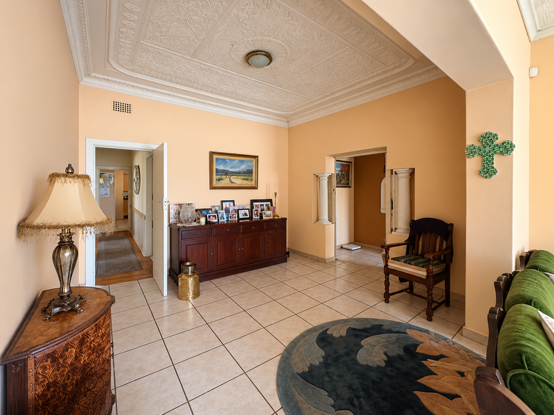 Spacious living area featuring an ornate pressed metal ceiling, ceramic floor tiles, and decorative architectural columns leading to an adjacent hallway.