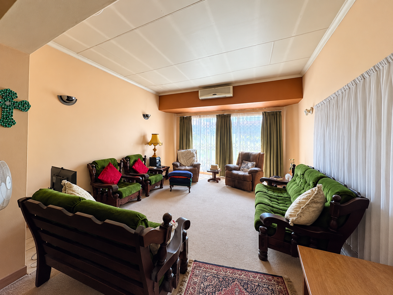 A spacious living room featuring neutral walls, carpeted flooring, and a wall-mounted air conditioning unit, offering a comfortable and functional layout.