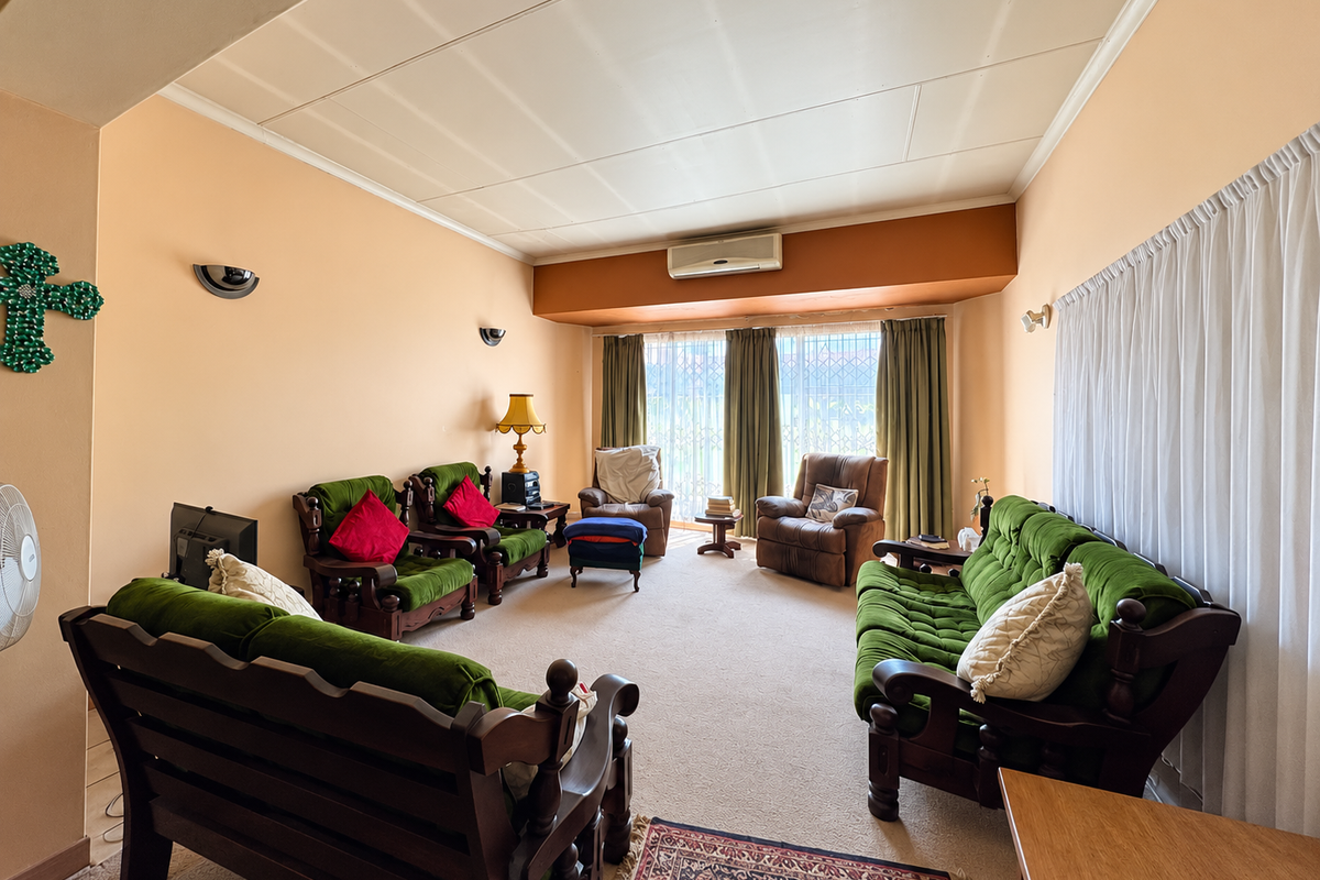 A spacious living room featuring neutral walls, carpeted flooring, and a wall-mounted air conditioning unit, offering a comfortable and functional layout.