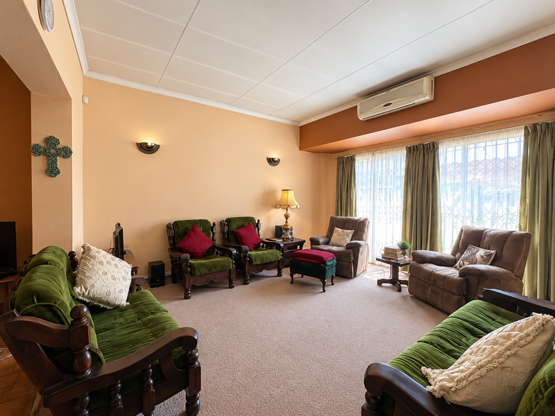A spacious living room featuring wall-mounted air conditioning, wall sconces, and large sliding glass doors with security gates, providing access to the exterior.