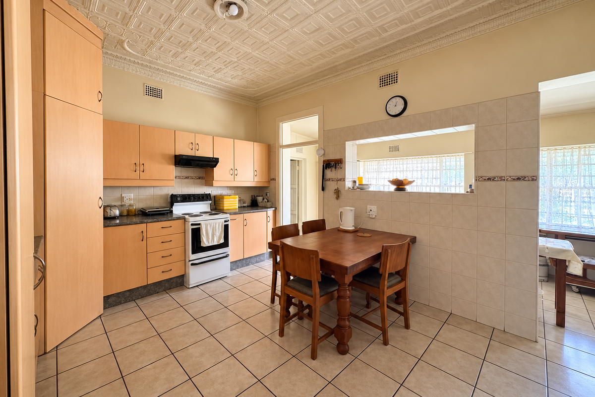 A functional kitchen featuring light wood cabinetry, tiled flooring, a decorative ceiling, and a convenient serving hatch opening into the adjacent living area.