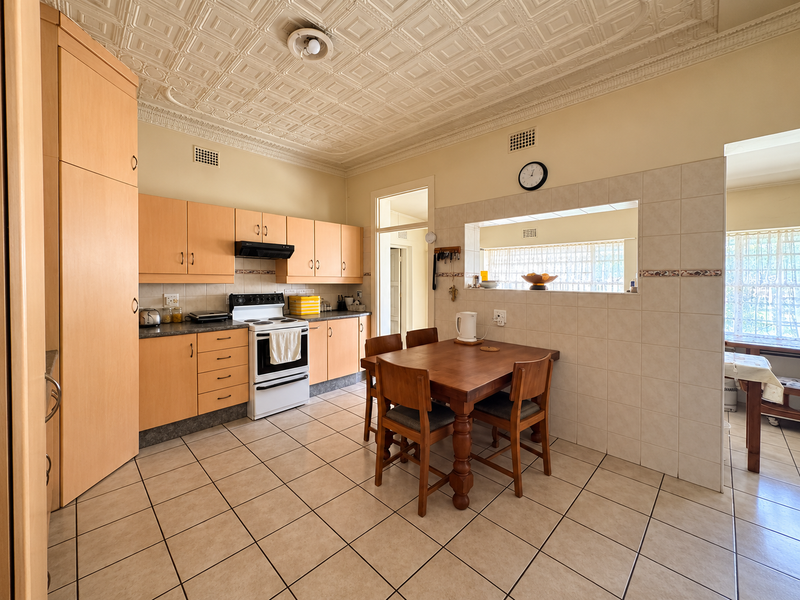 A functional kitchen featuring light wood cabinetry, tiled flooring, a decorative ceiling, and a convenient serving hatch opening into the adjacent living area.