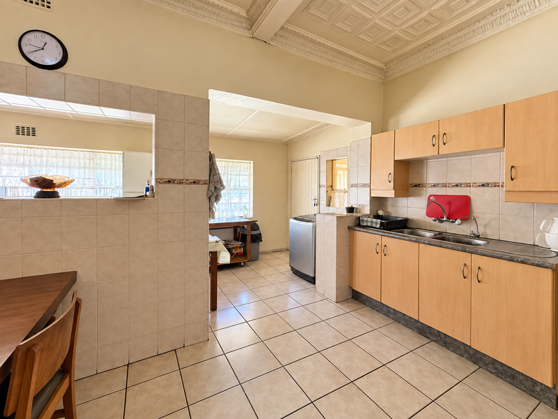 Functional kitchen featuring light wood cabinetry, tiled splashbacks, and a double sink, with an adjacent utility area and decorative ceiling detail.
