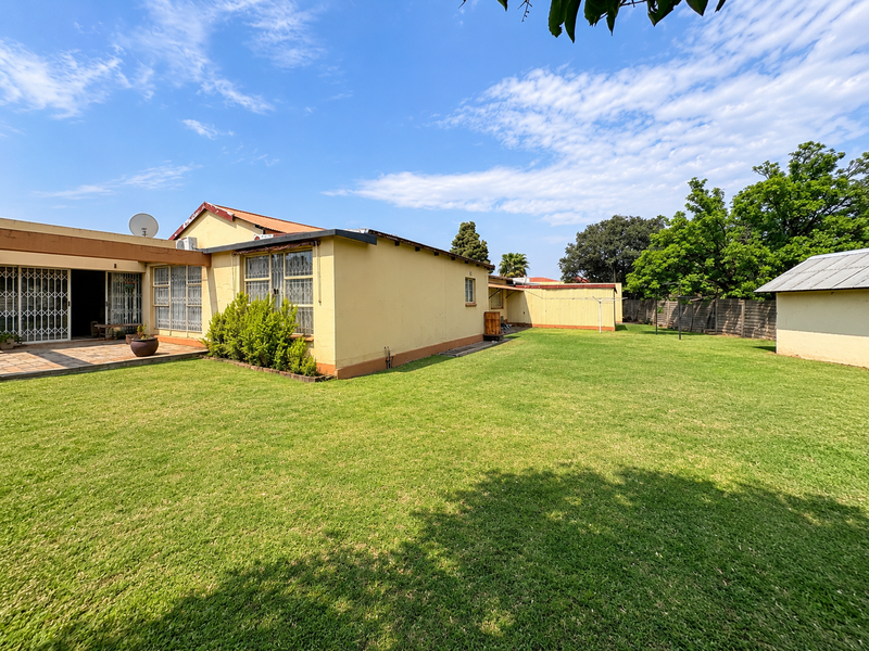 Spacious rear garden featuring a large lawn, a covered patio area with security gates, and a detached outbuilding.