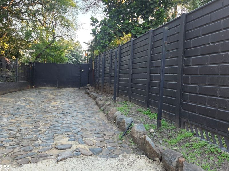 A private driveway entrance featuring a cobblestone surface, enclosed by a dark perimeter wall and a secure metal gate.