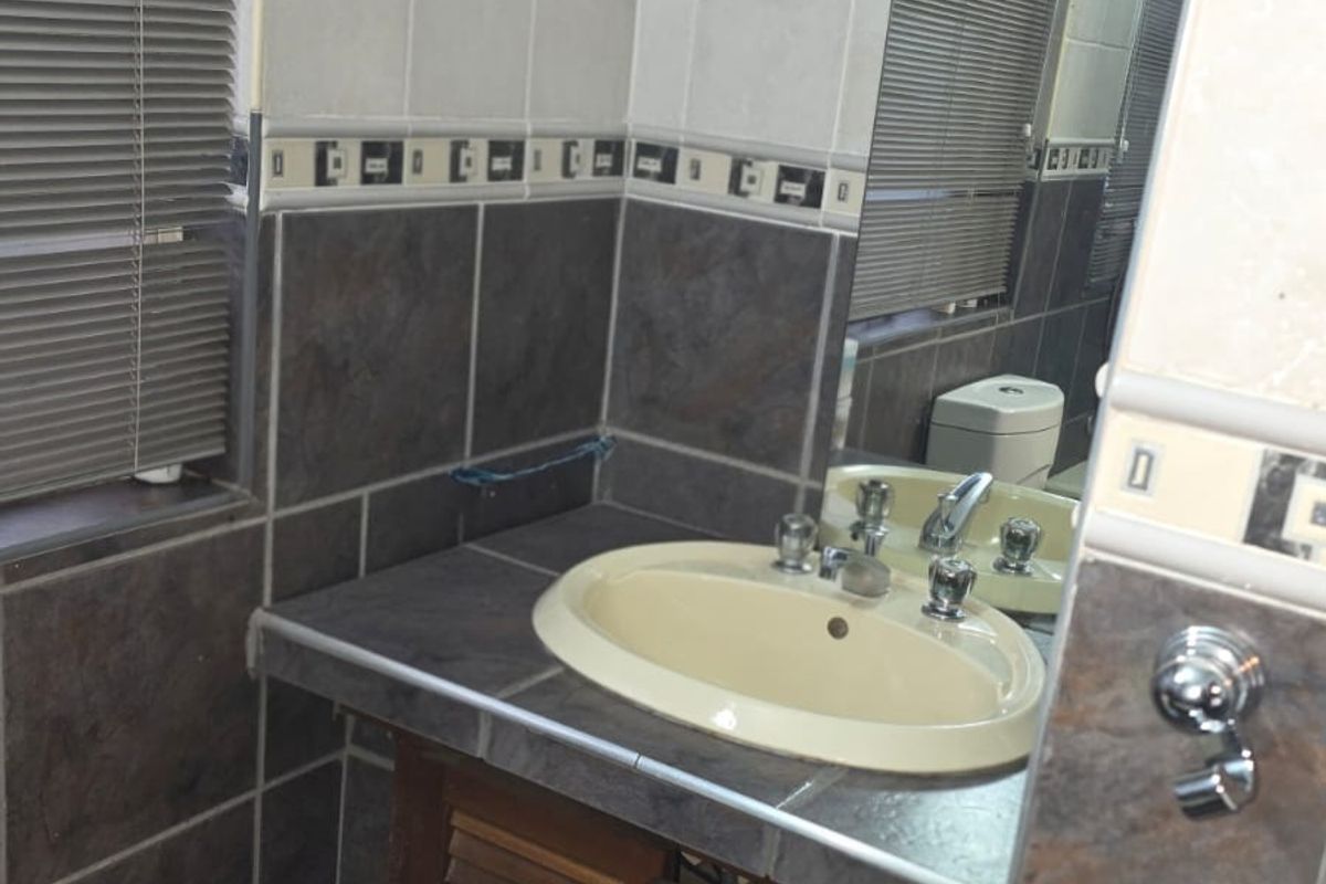 A functional bathroom featuring a vanity cabinet with a drop-in basin, tiled splashbacks, and a wall-mounted mirror.