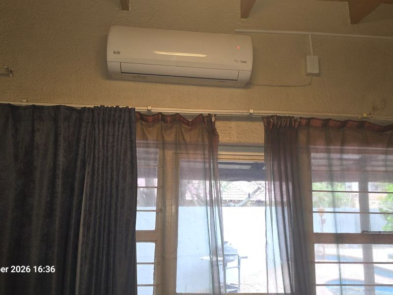 Living area featuring exposed timber beams and a wall-mounted air conditioning unit, showing signs of wall staining and surface-mounted electrical wiring.