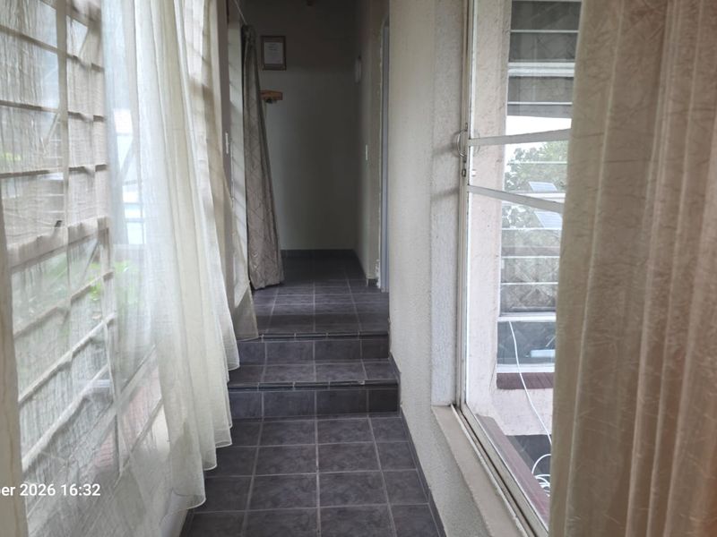 A tiled hallway featuring a stepped transition and large sliding windows, providing a bright and functional passage between living areas.