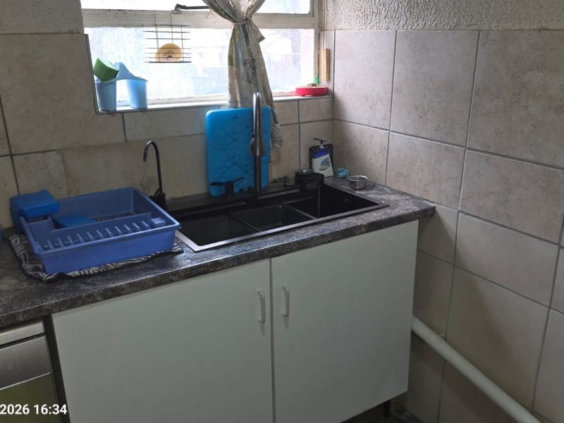 A functional scullery area featuring a double sink, laminate countertop, and tiled splashback, providing essential utility space for food preparation and cleaning.