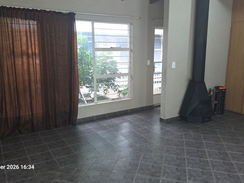 Spacious living area featuring dark tiled flooring, a built-in fireplace, and large windows with security bars, offering a clean and functional blank canvas.