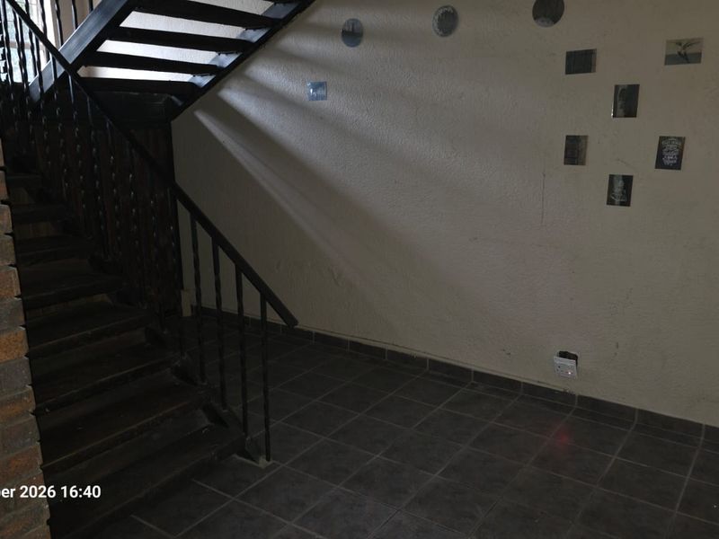 An interior hallway featuring a staircase with a metal balustrade, tiled flooring, and an exposed brick wall section.