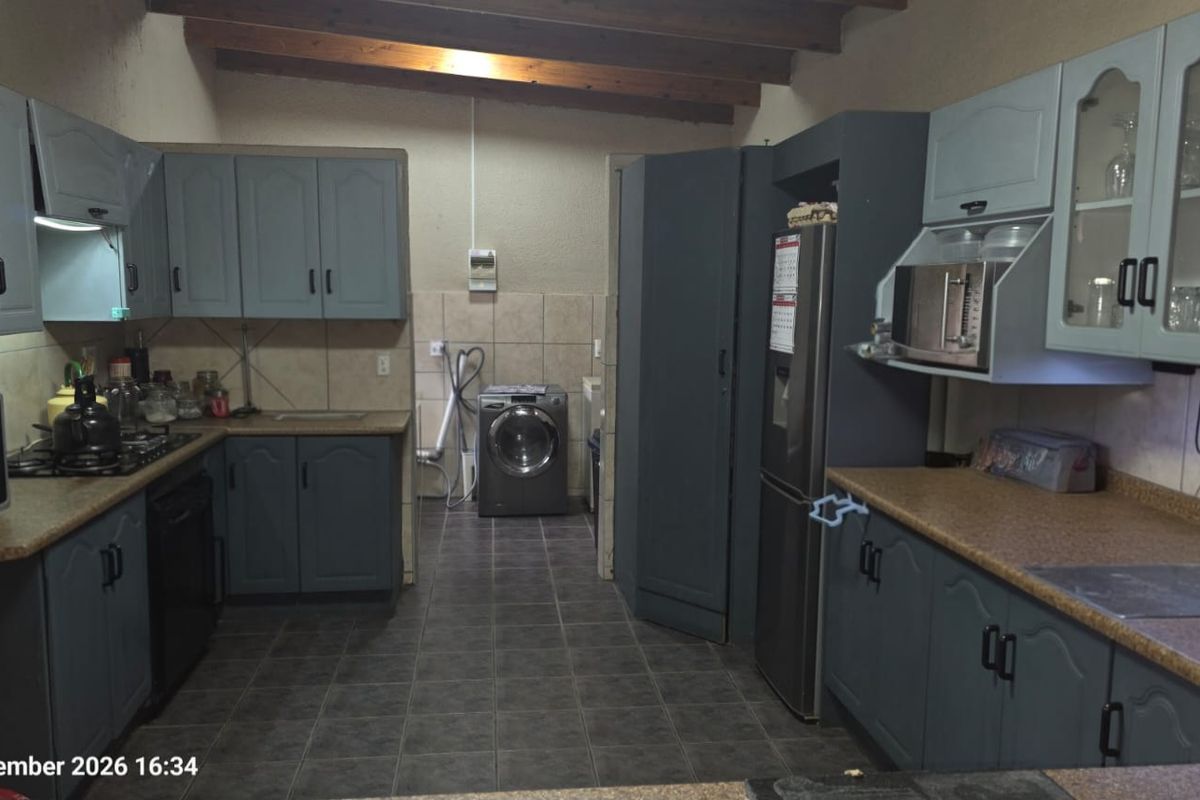 A functional kitchen featuring built-in cabinetry, laminate countertops, a gas hob, and exposed timber ceiling beams, with integrated laundry plumbing connections.