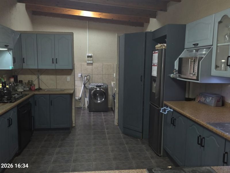 A functional kitchen featuring built-in cabinetry, laminate countertops, a gas hob, and exposed timber ceiling beams, with integrated laundry plumbing connections.
