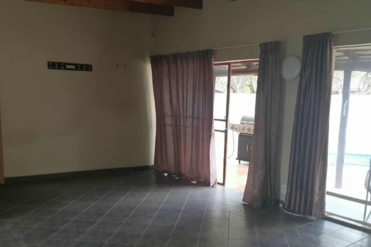 Spacious living area featuring tiled flooring, exposed timber ceiling beams, and a built-in fireplace, with direct access to the outdoor patio area.