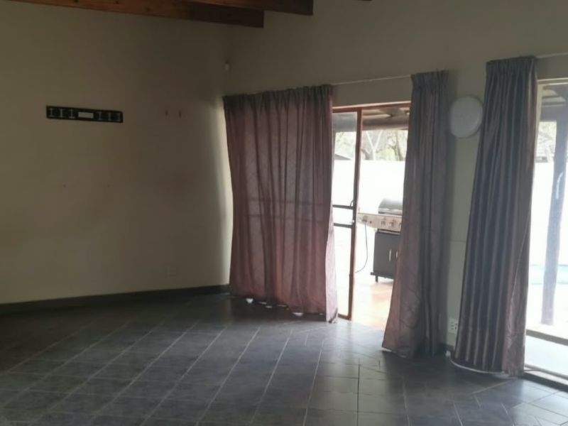 Spacious living area featuring tiled flooring, exposed timber ceiling beams, and a built-in fireplace, with direct access to the outdoor patio area.