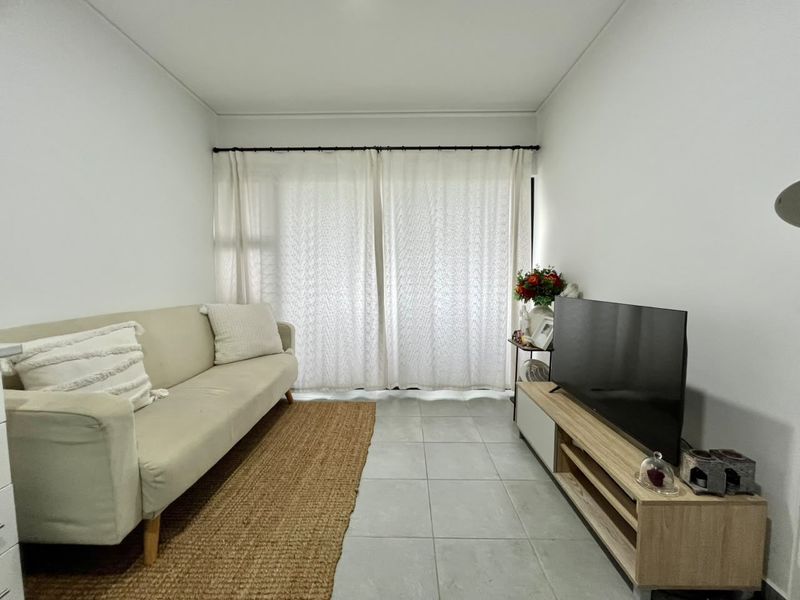 A neutrally decorated living room featuring tiled flooring and large window curtains, providing a bright and functional space.