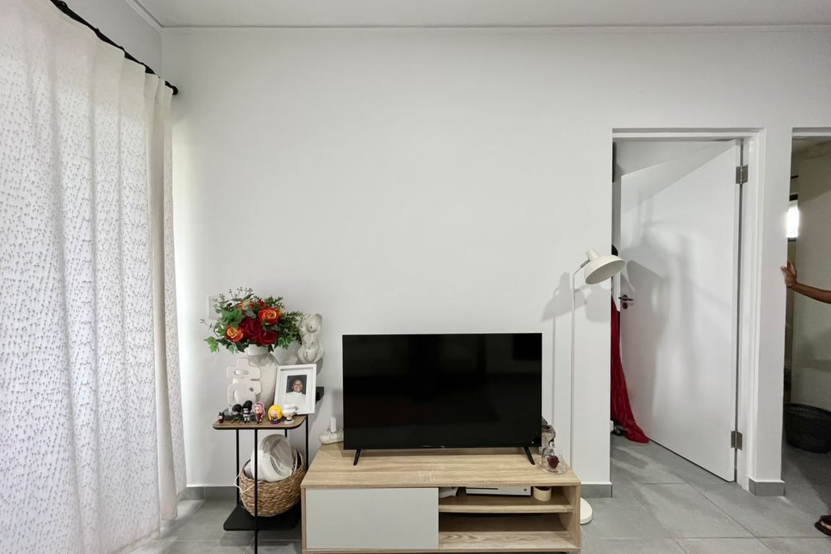 A living room area featuring neutral tiled flooring, a white interior door, and a curtain rod, providing a clean and functional space.
