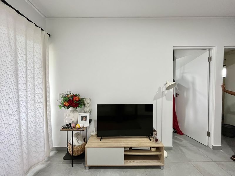 A living room area featuring neutral tiled flooring, a white interior door, and a curtain rod, providing a clean and functional space.