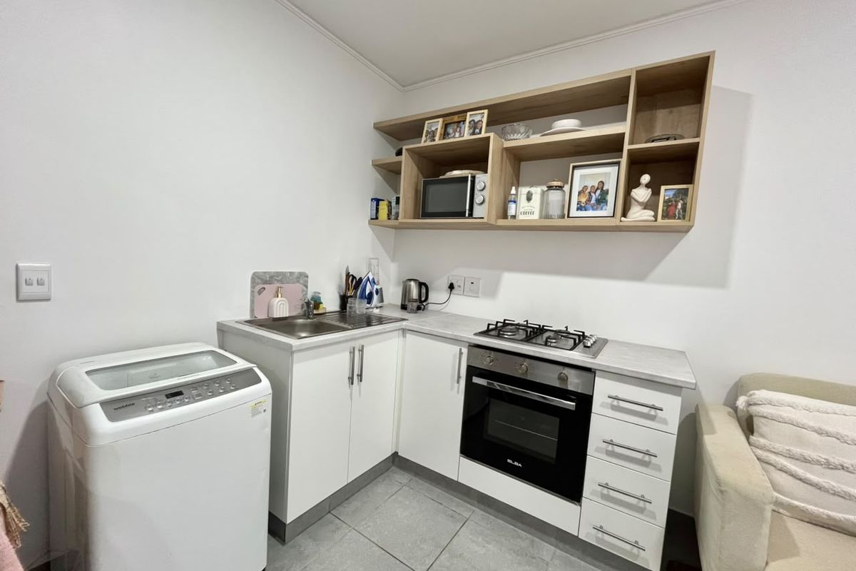 Compact kitchen featuring white cabinetry, gas hob, built-in oven, stainless steel sink, and open shelving, finished with tiled flooring.