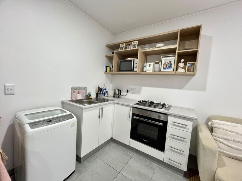 Compact kitchen featuring white cabinetry, gas hob, built-in oven, stainless steel sink, and open shelving, finished with tiled flooring.