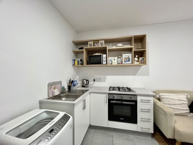 Compact kitchen area featuring white cabinetry, stainless steel sink, built-in oven, gas cooktop, and open shelving for storage.