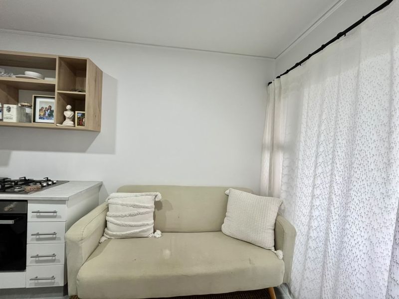 Compact open-plan living area featuring a built-in oven, gas cooktop, and integrated kitchen cabinetry with open shelving.