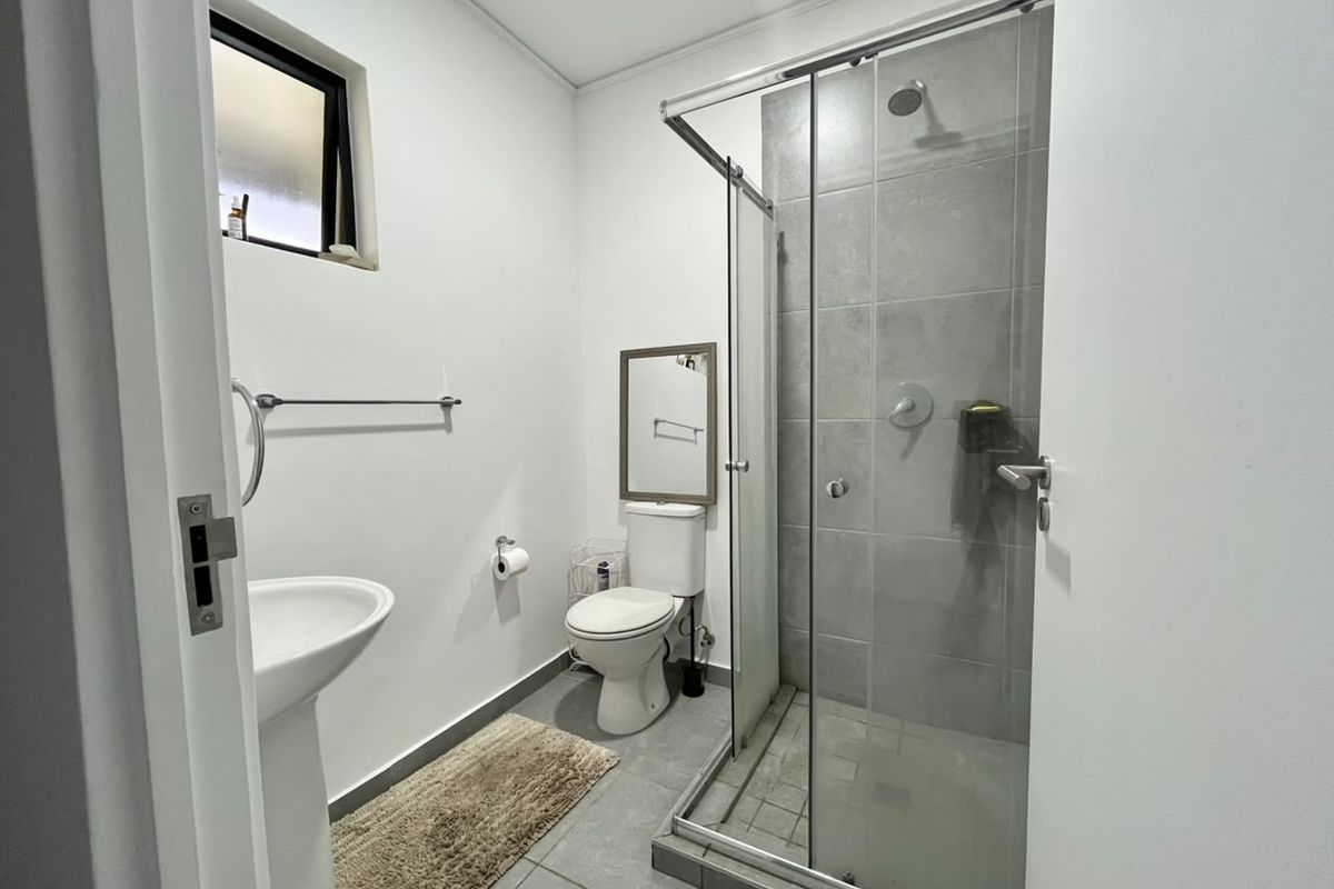 A clean and functional bathroom featuring a pedestal basin, toilet, and a glass-enclosed shower with grey tiled finishes.
