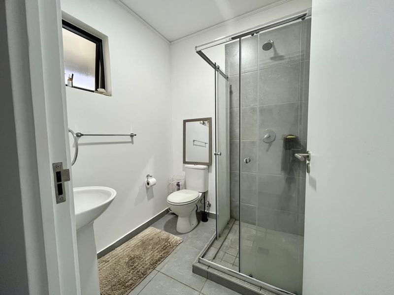 A clean and functional bathroom featuring a pedestal basin, toilet, and a glass-enclosed shower with grey tiled finishes.