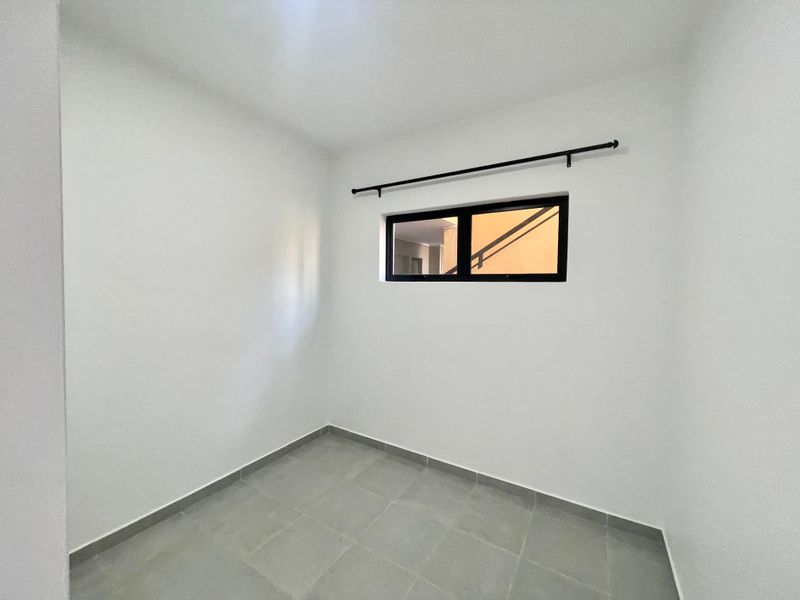 A clean, empty bedroom featuring neutral tiled flooring, white walls, and a modern black-framed window with an installed curtain rod.