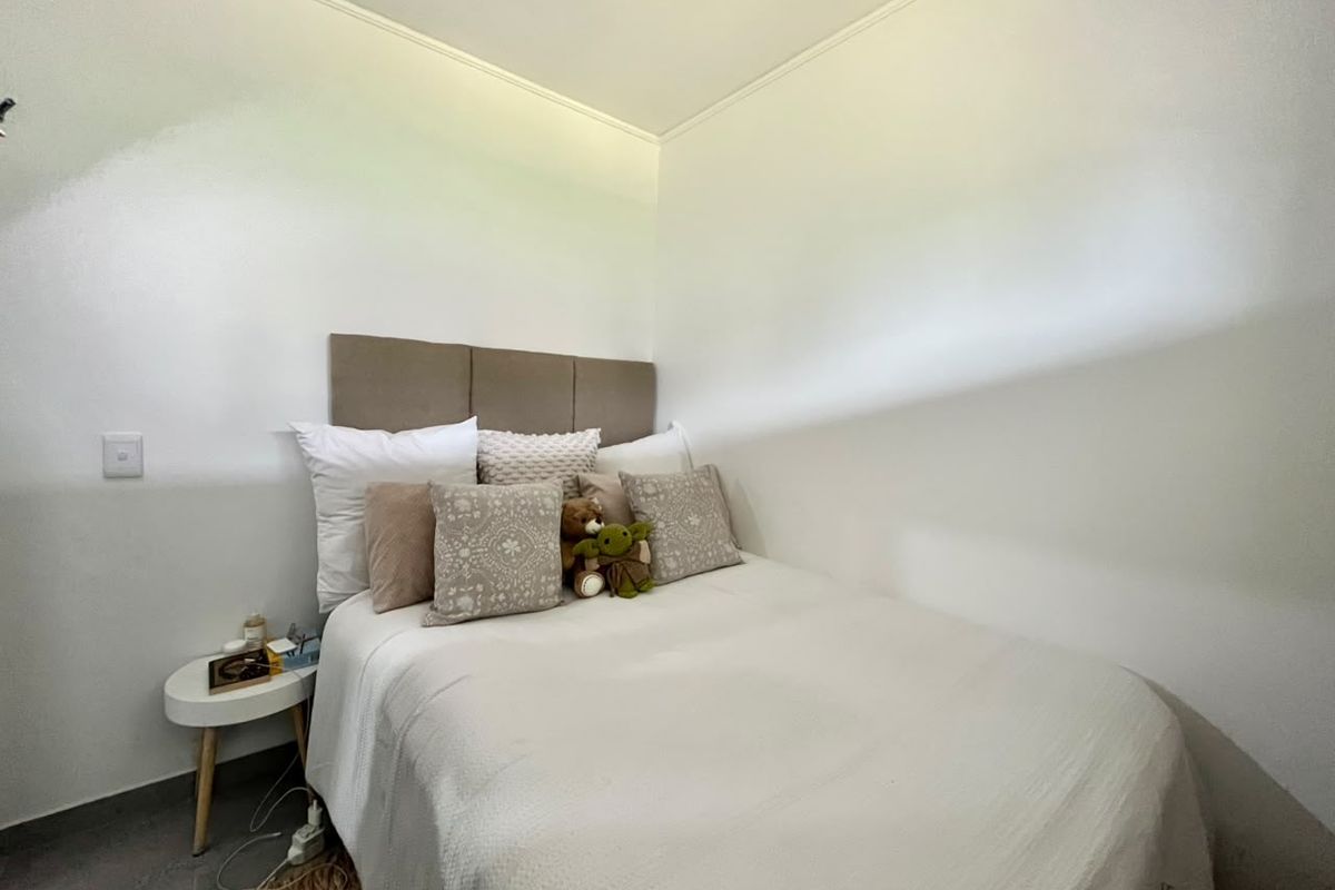 A compact bedroom featuring a neutral color palette and a built-in upholstered headboard, providing a simple and functional sleeping space.