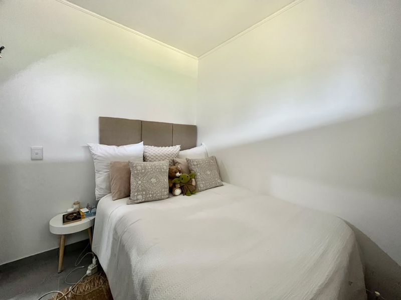 A compact bedroom featuring a neutral color palette and a built-in upholstered headboard, providing a simple and functional sleeping space.