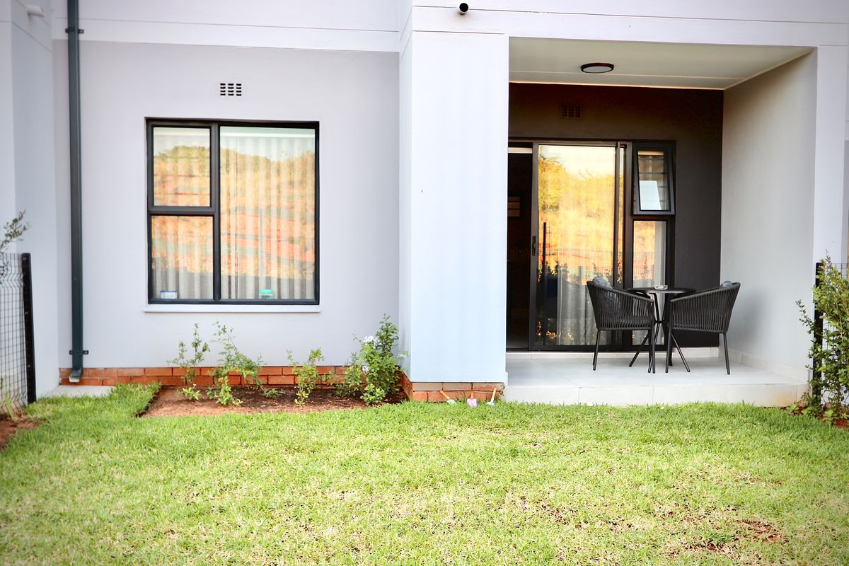Rear view of the apartment featuring a covered patio, landscaped garden area, and modern aluminium-framed windows and sliding doors.