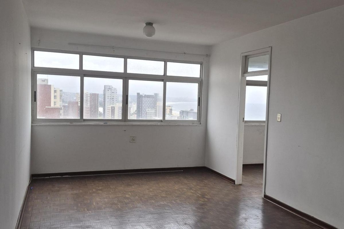 An empty living room featuring original parquet flooring, large windows with city views, and neutral wall finishes, offering a blank canvas for renovation.