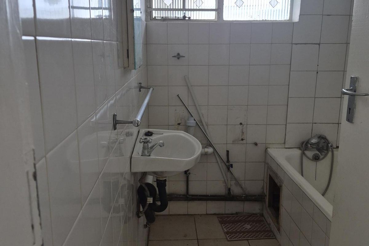 A dated bathroom featuring a wall-mounted basin, bathtub, and tiled finishes, currently requiring significant renovation and repair to modernize the space.