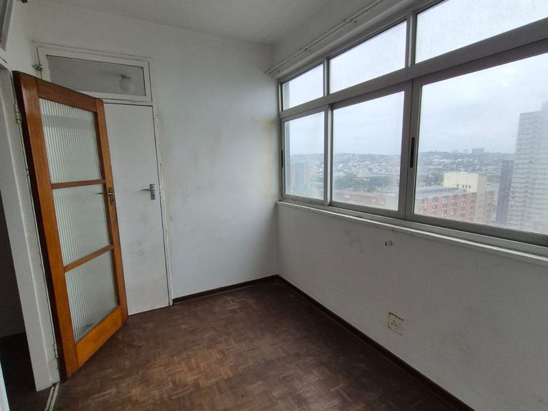 An enclosed balcony or sunroom featuring parquet flooring, large windows with city views, and a timber-framed glass door.
