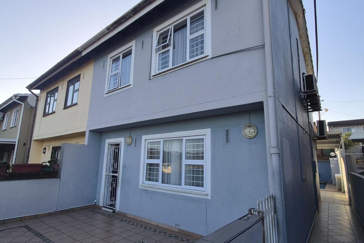 Rear exterior view of a two-story house featuring a tiled patio area, security gate, and external air conditioning unit.