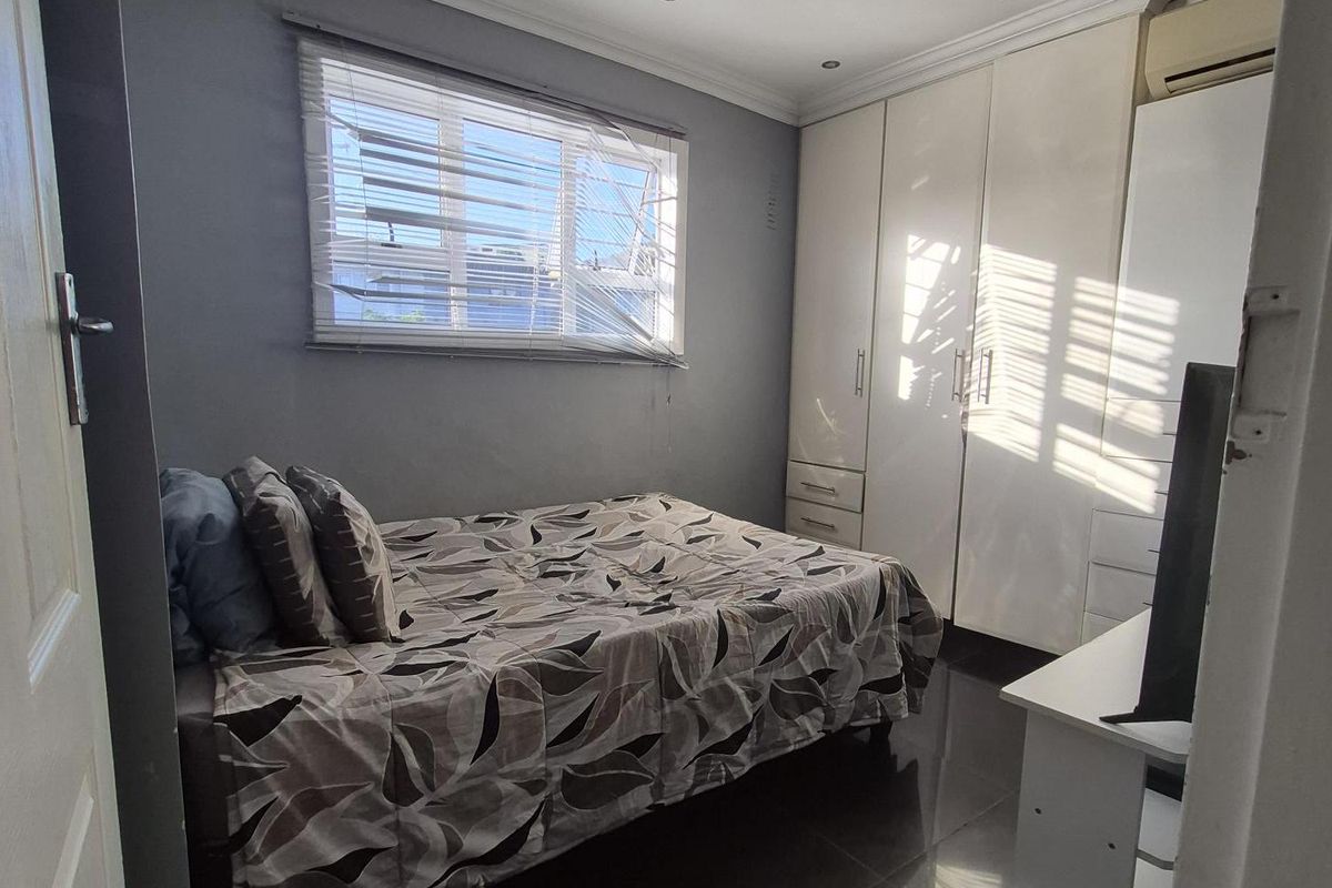 A compact bedroom featuring built-in cupboards, tiled flooring, recessed downlighting, and an integrated air conditioning unit.
