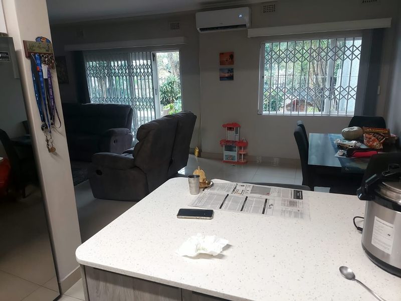 Open-plan living and dining area featuring tiled flooring, a kitchen island, and split-system air conditioning with security gates on windows and doors.