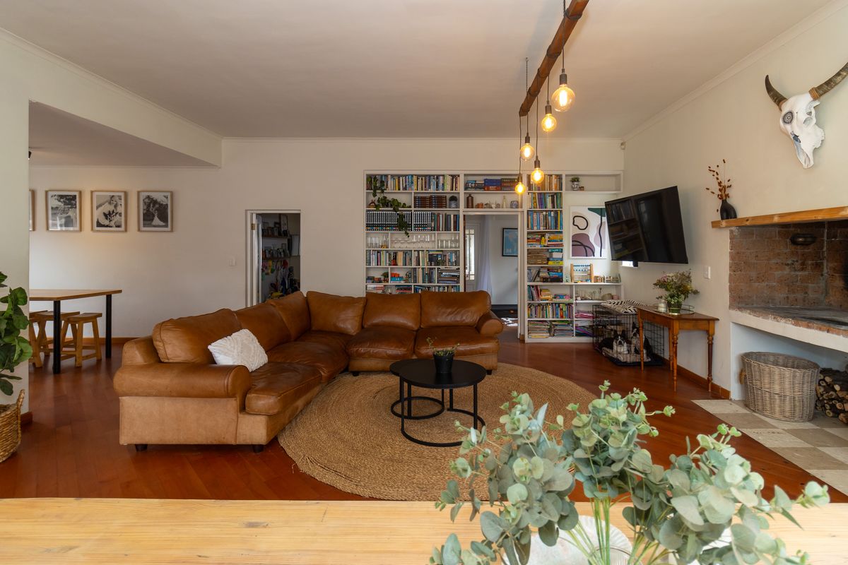 Spacious living room featuring warm timber flooring, a characterful brick fireplace, and extensive built-in shelving, creating a comfortable and inviting family space.