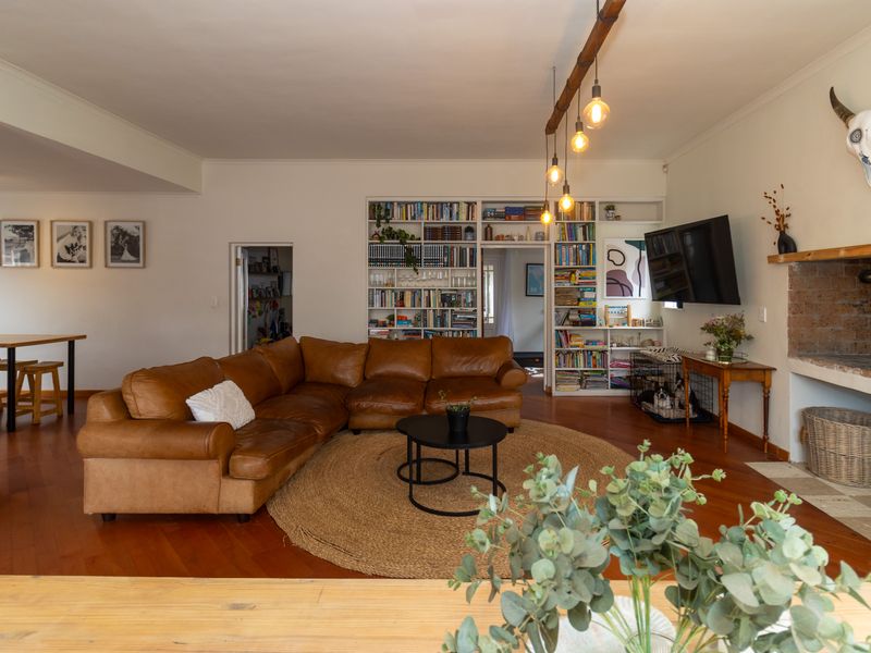 Spacious living room featuring warm timber flooring, a characterful brick fireplace, and extensive built-in shelving, creating a comfortable and inviting family space.
