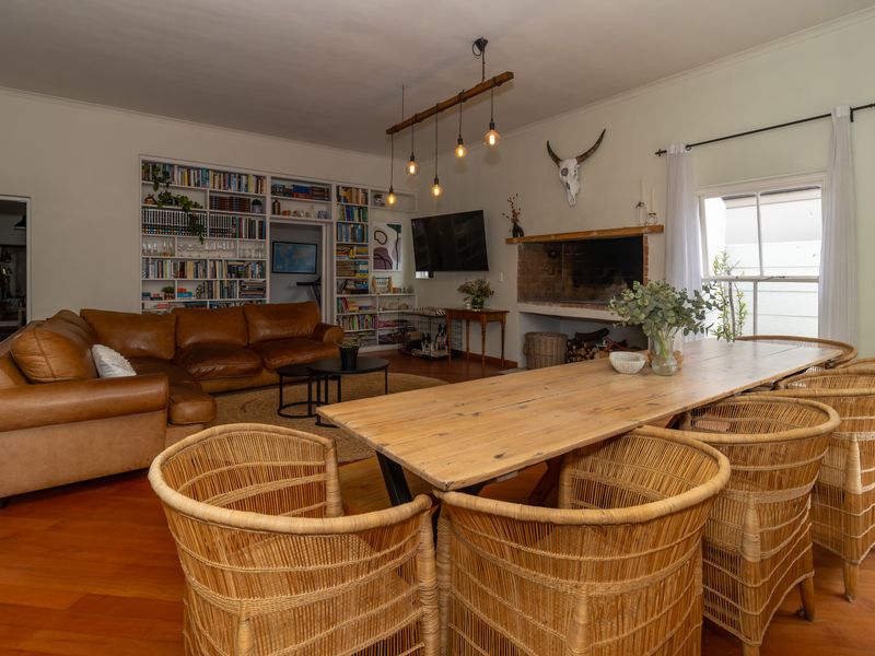Spacious open-plan living and dining area featuring warm wooden flooring, a classic brick fireplace, and extensive built-in shelving.