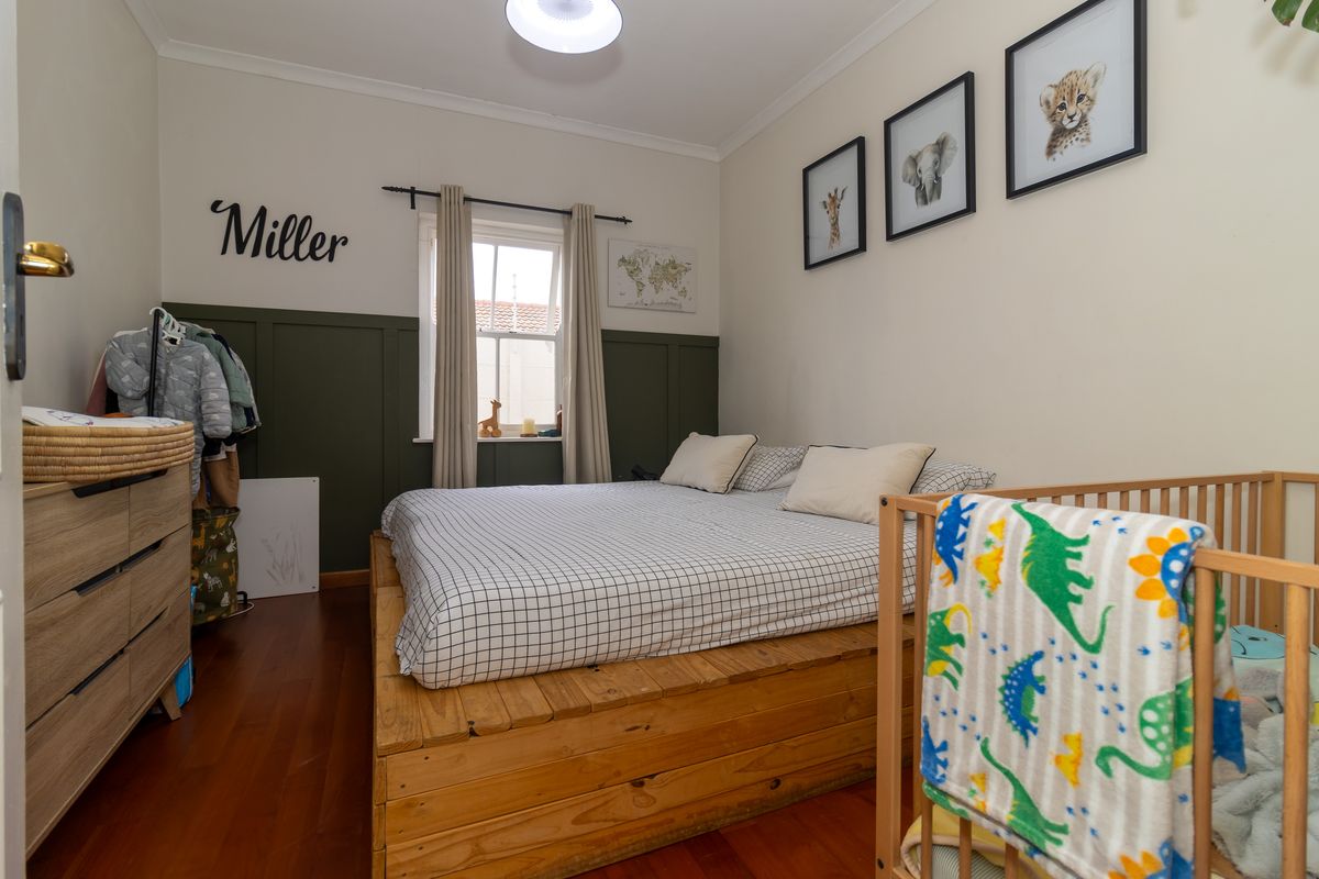 A well-maintained bedroom featuring timber flooring, a sash window, and decorative wainscoting, providing a cozy and functional living space.