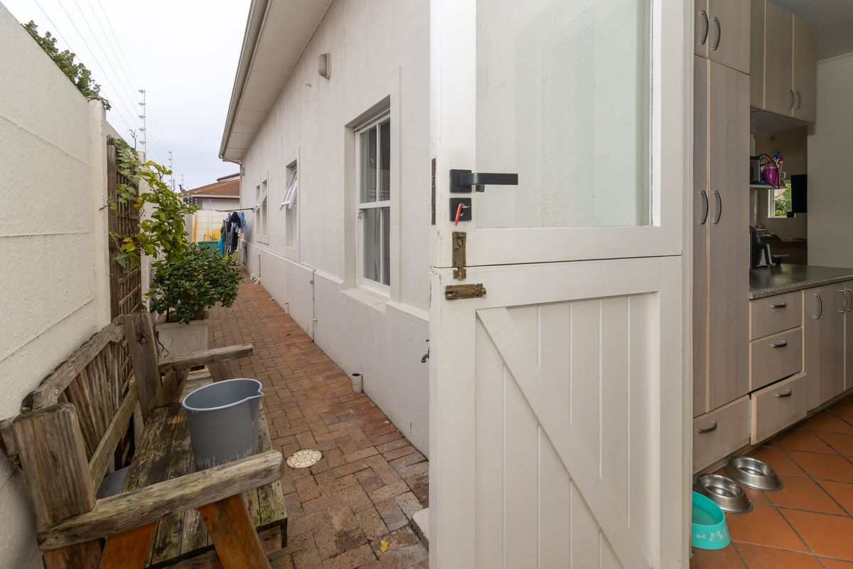 A view of the rear exterior brick-paved walkway leading into the kitchen area through a white stable door.