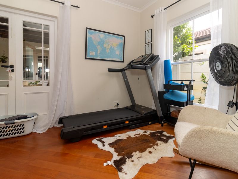 A functional home gym space featuring polished hardwood flooring, classic french doors, and large sash windows providing natural light.